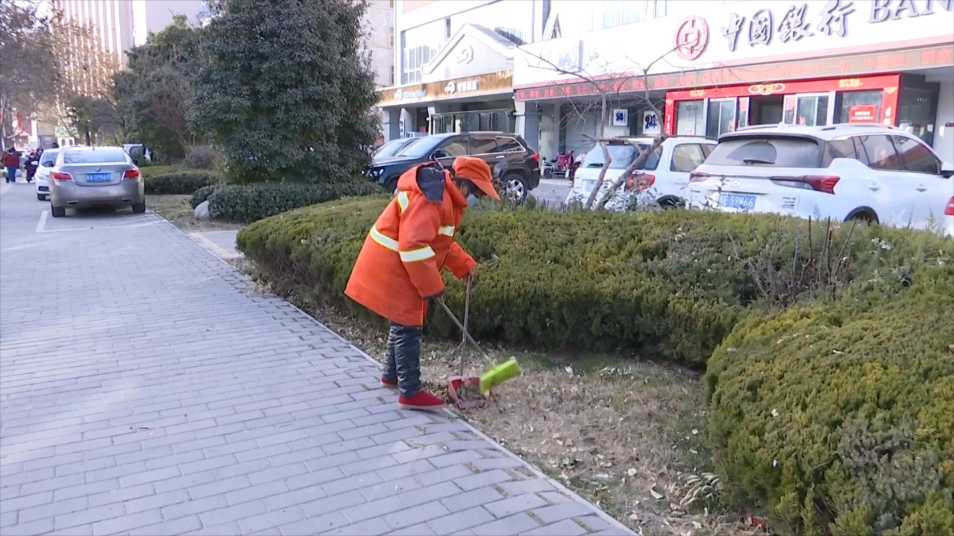 图为:环卫工人闫绒利正在对绿化带进行清扫保洁