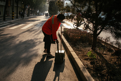 图为:陕西省渭南市临渭区,清晨在东风大街路边扫地的环卫工人