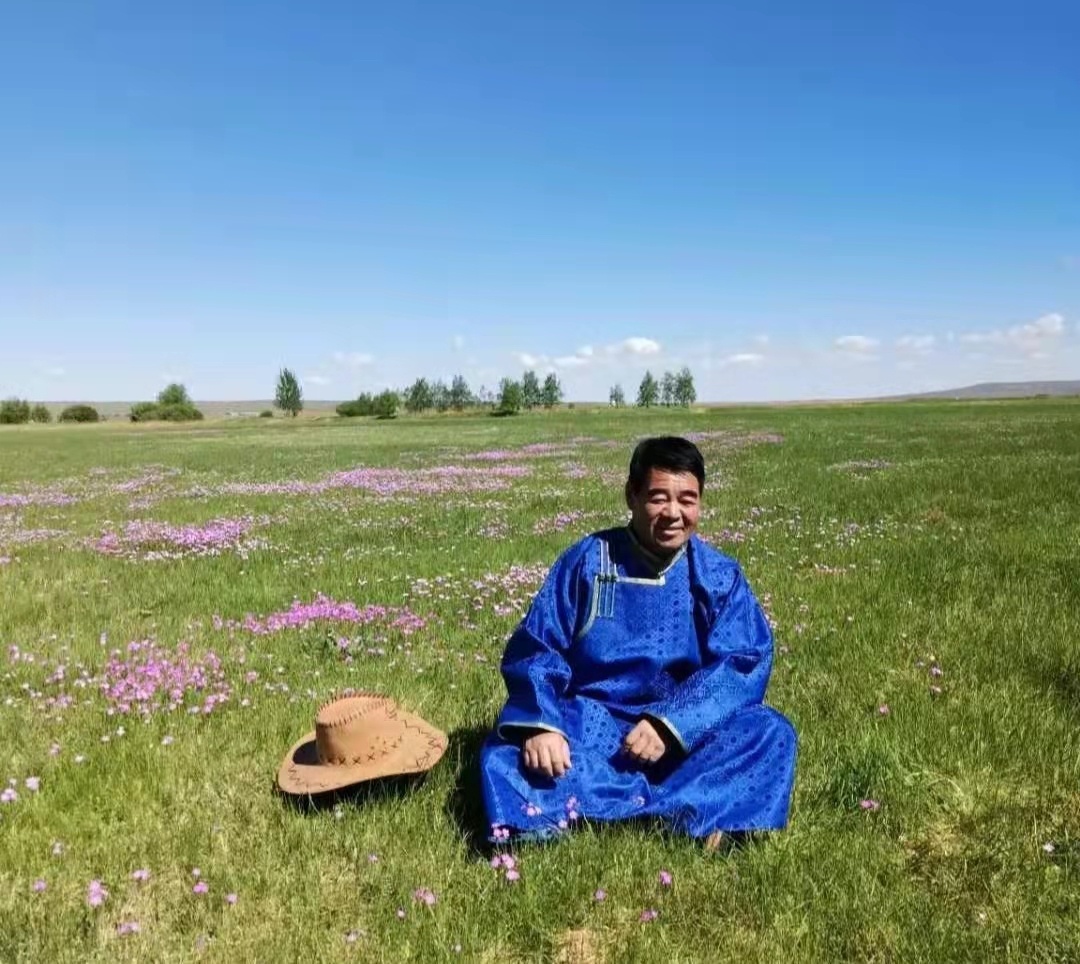 端坐在花草茂盛的草原上，看着牧民的腰包越来越鼓，廷·巴特尔笑得很开心。（摄影：张重阳）